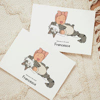Two custom horizontal birth announcement cards on a textured cream rug. The hand-drawn vector illustration shows a laughing baby wearing a pink bow headband and a cream romper, holding a large, fluffy gray and white tabby cat on its back. The text below reads "Welcome to the world Francesca"