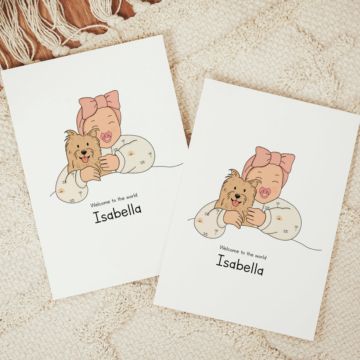 Two vertical personalized baby announcement cards on a beige fringe rug. The vector design shows a smiling baby wearing a large pink bow headband and a cream romper patterned with tiny palm trees and suns, cuddling a small, shaggy brown terrier dog. The text reads "Welcome to the world Isabella"
