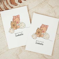 Two vertical personalized baby announcement cards on a beige fringe rug. The vector design shows a smiling baby wearing a large pink bow headband and a cream romper patterned with tiny palm trees and suns, cuddling a small, shaggy brown terrier dog. The text reads "Welcome to the world Isabella"