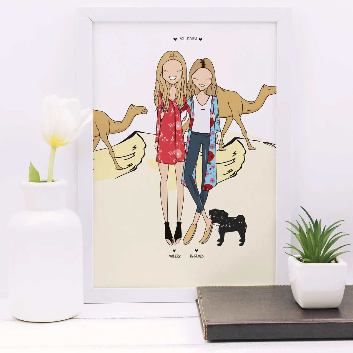 Personalized family portrait with custom background of a desert safari with camels, showcasing two friends and a pet pug as a unique birthday or travel memory gift. The women are wearing colourful dresses and are standing in front of two camels. The text "Soulmates" is at the top of the image. The names "Wiley" and "Marbles" are written below the women.