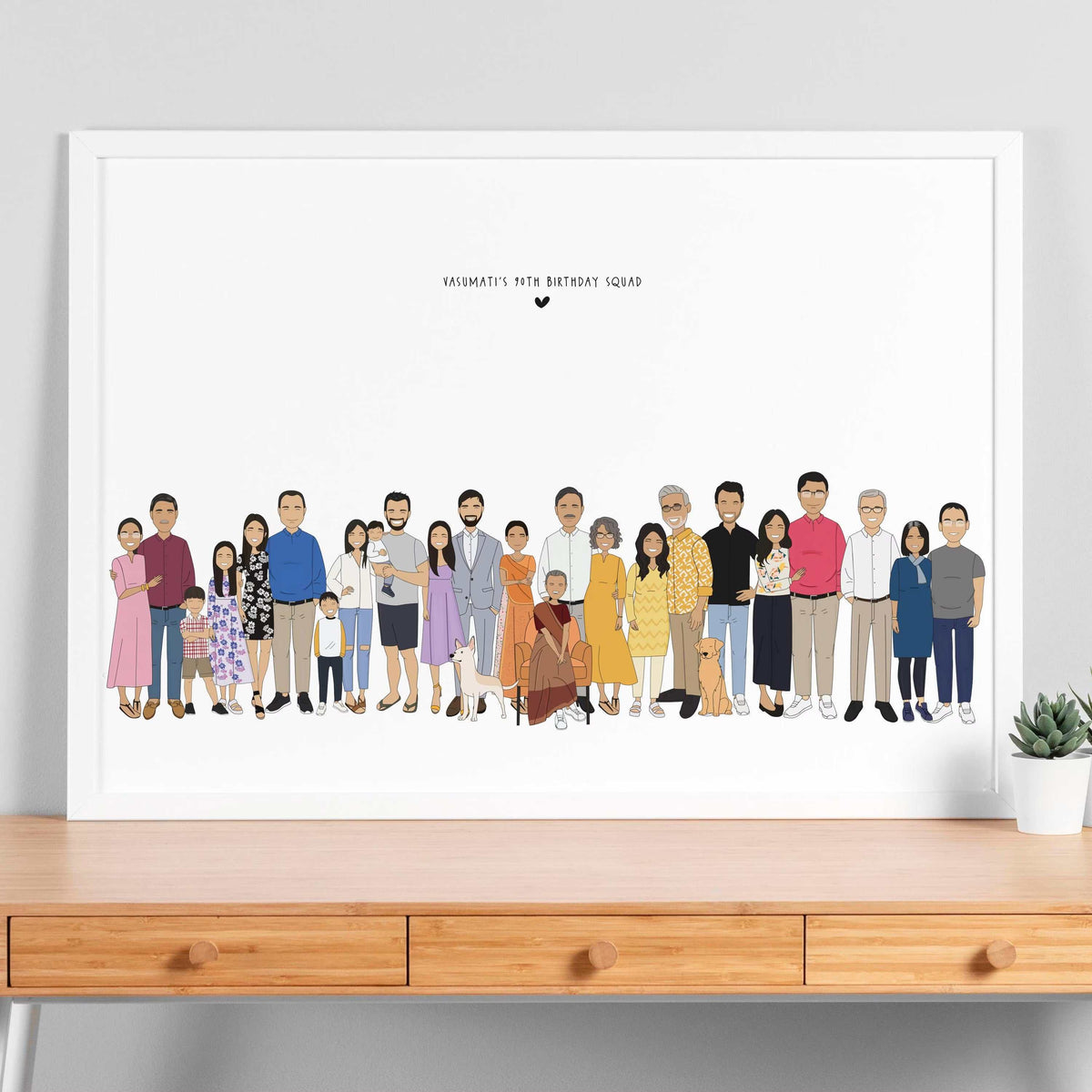 A cartoon illustration of an extended South Asian family and their pets in a white frame. There are thirty people in the family. A woman in a red-orange sari sits in an armchair at the center, surrounded by her family. One brown dog and one white cat sit near her. Above them, text reads: "VASUMATI'S 90th BIRTHDAY SQUAD," with a black heart.