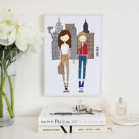 A framed illustration of two women standing together in front of a cityscape. The women are holding hands and are wearing casual clothing. The cityscape is of New York City and includes the Statue of Liberty and skyscrapers. The text "NEW YORK" is written vertically on the right side of the image. The names "BRANDE" and "HELEN" are written below the women. Perfect as a New York travel souvenir, moving away gift, or a birthday keepsake for a travel partner.
