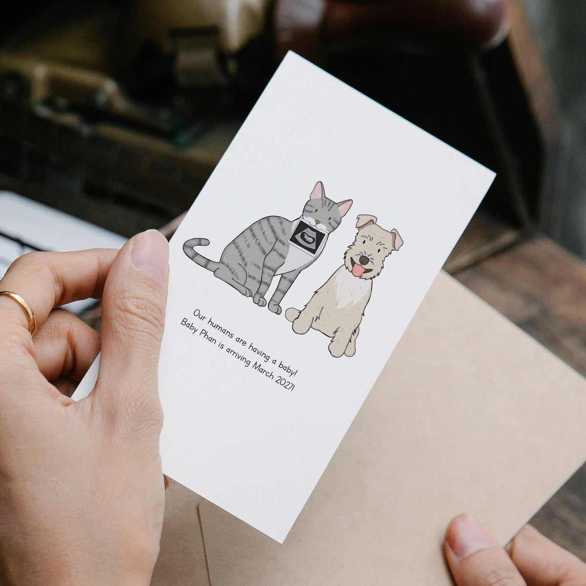 Personalized Pregnancy Announcement Card featuring a Custom Hand Painted Pet Portrait of a grey tabby cat holding in his mouth an ultrasound and a Mini Schnauzer dog smiling with a kraft envelope.