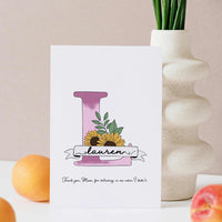A hand-drawn Mother’s Day card featuring a large violet floral initial "L" decorated with sunflowers and green leaves. A white banner across the letter displays the name "Lauren" in elegant script. At the bottom, a heartfelt Mother's Day quote. This personalized A5 thank you gift has a clean, artistic feel, perfect for a sentimental keepsake.