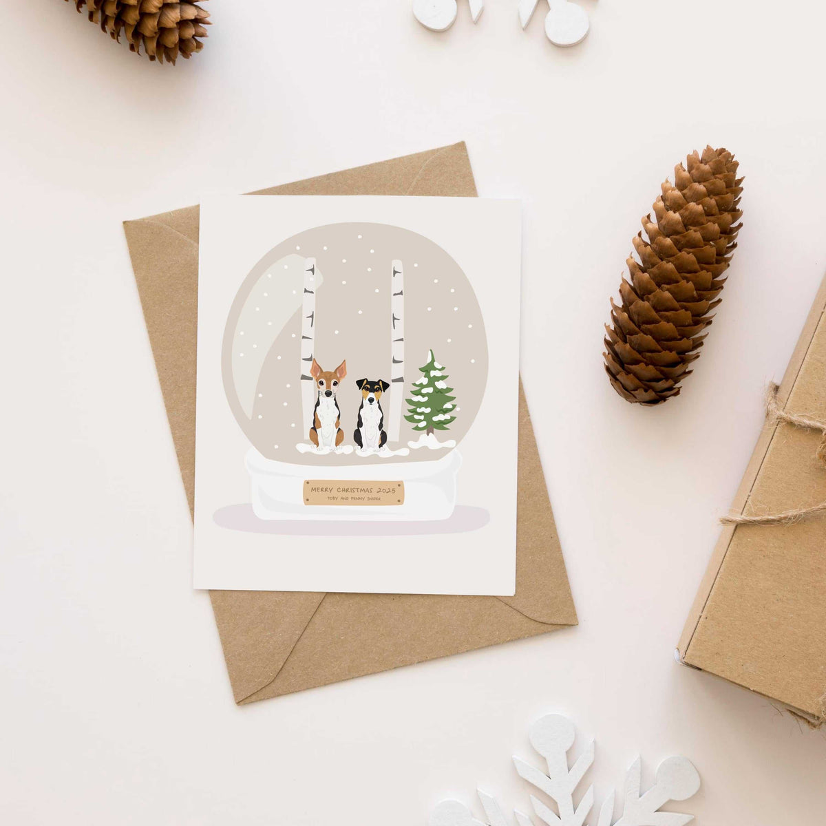 Two custom hand-drawn terrier dogs inside a snow globe illustration on a Personalized Pet Portrait for Christmas Card displayed on a rustic holiday envelope.