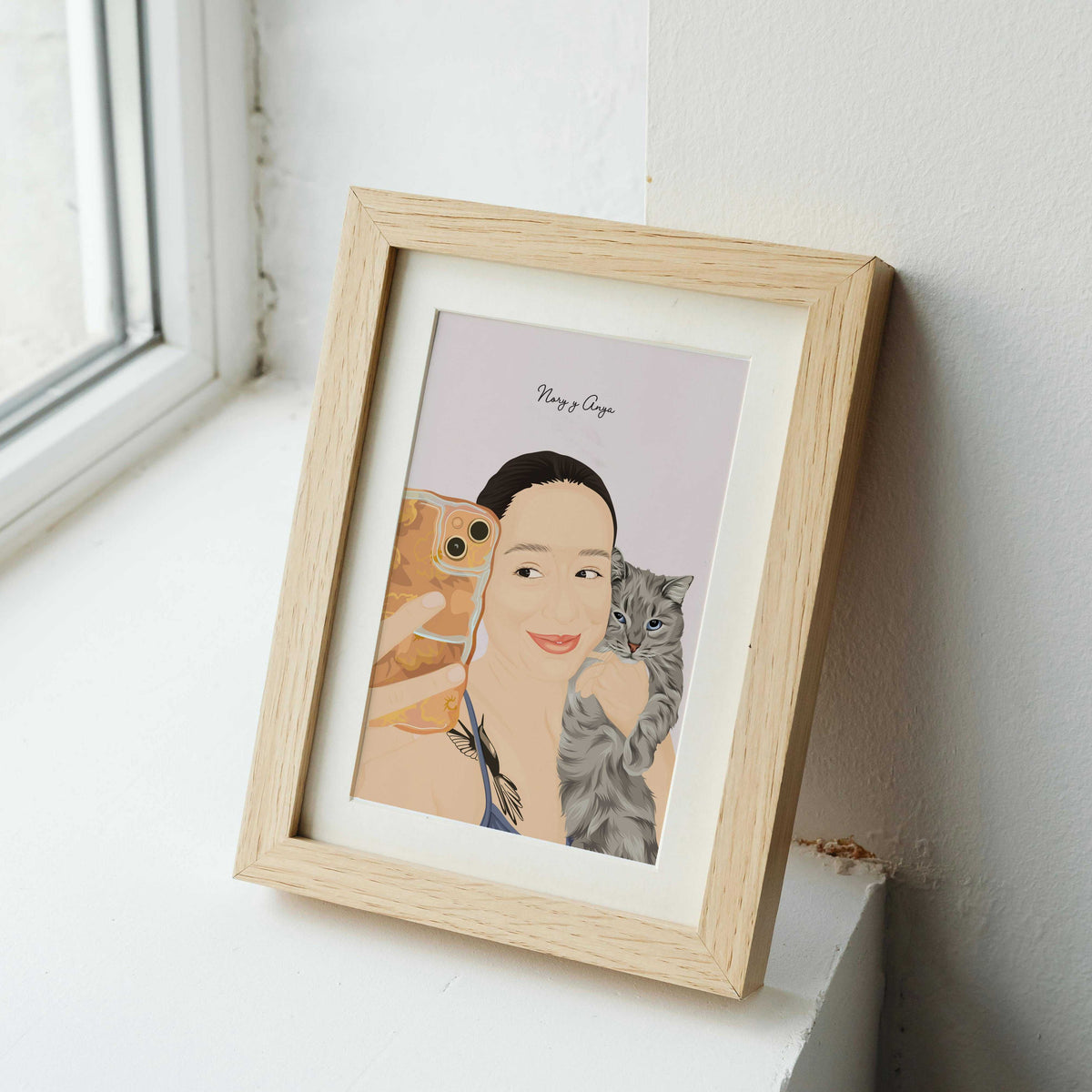A personalized pet and owner portrait showing a woman taking a mirror selfie while holding her grey tabby cat, displayed in a light wood frame as a unique birthday gift for a cat lover.