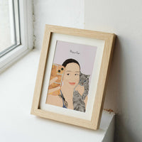 A personalized pet and owner portrait showing a woman taking a mirror selfie while holding her grey tabby cat, displayed in a light wood frame as a unique birthday gift for a cat lover.