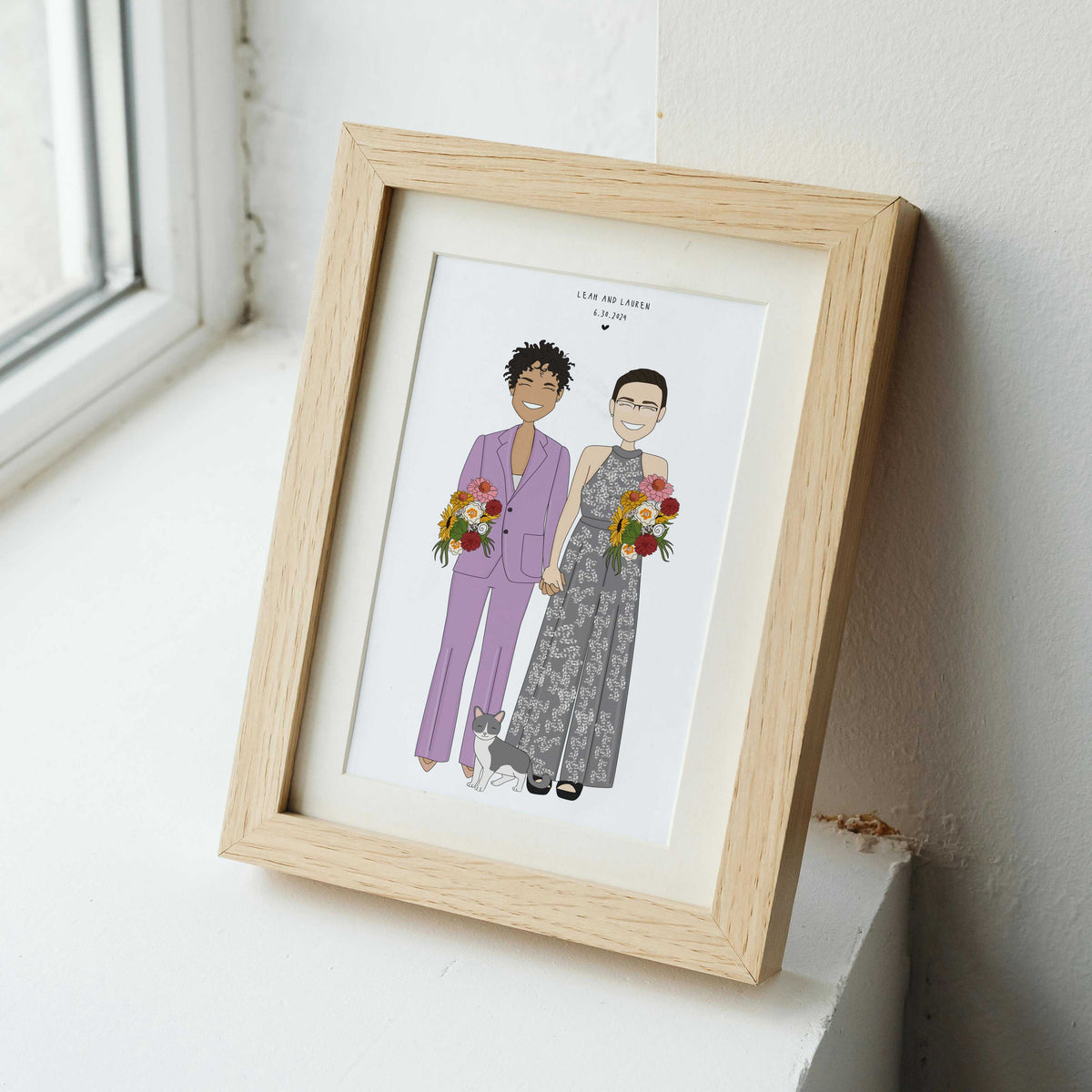 Personalized LGBTQ+ wedding portrait illustration of two brides and their cat, showcased in a light natural wood frame resting on a white window sill.